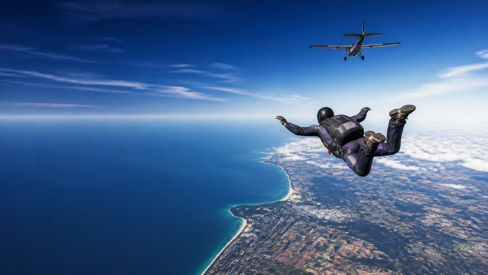A tandem skydiver in freefall above a blue coastline